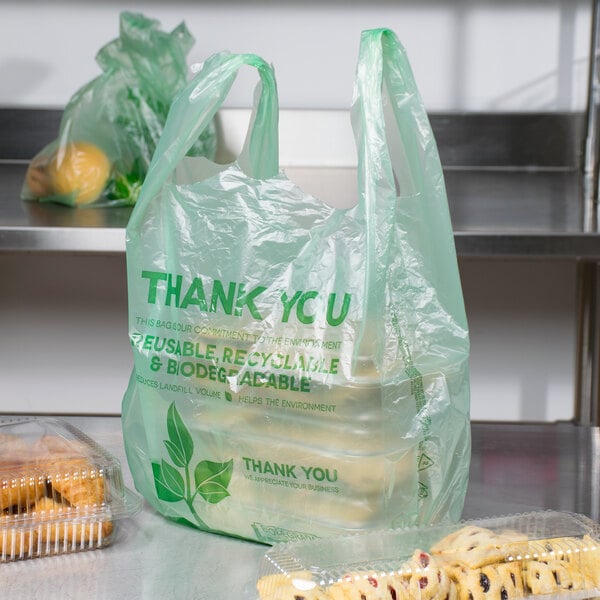 Green plastic t-shirt bag with various pastries in plastic containers surrounding it
