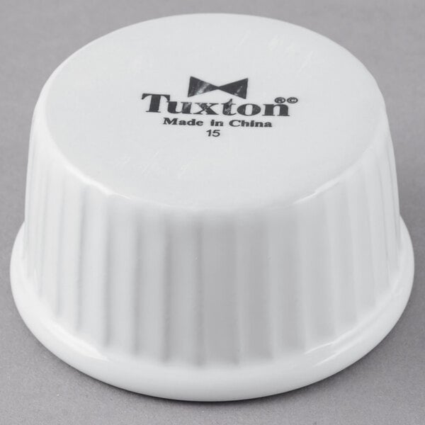 A Tuxton white fluted ceramic ramekin with black text on the side.