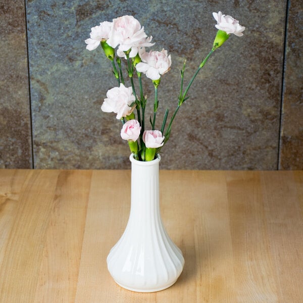 A white Cambro bud vase with pink flowers on a table.