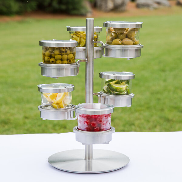 A Cal-Mil stainless steel rotating display stand with three jars of food with hinged lids.