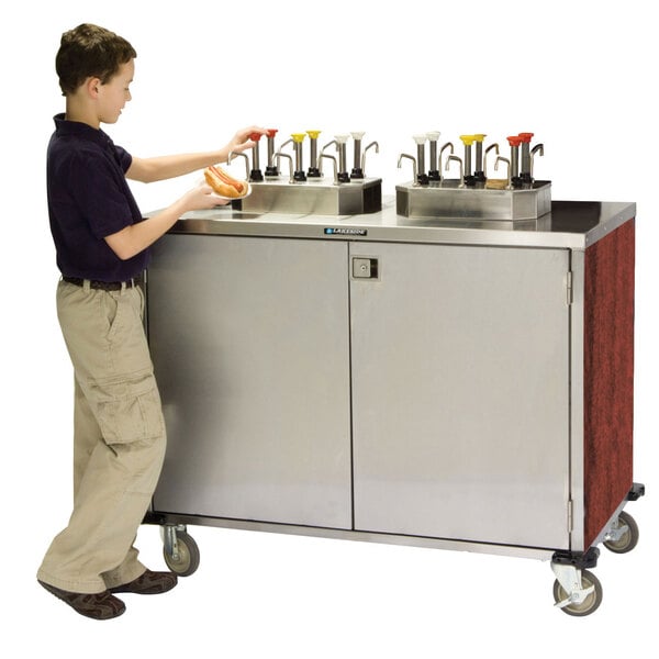 A young boy using a Lakeside stainless steel condiment cart.