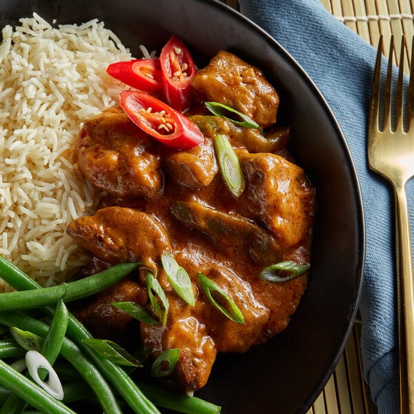 A bowl of rice and green beans with a plate of meat on a table.