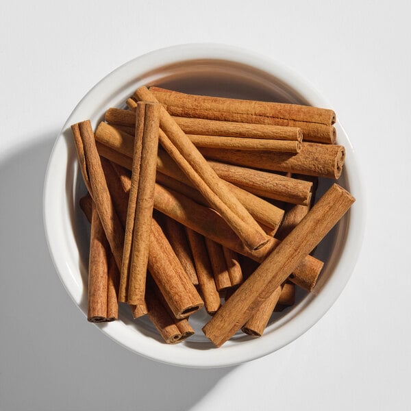 A white bowl filled with several whole cinnamon sticks.