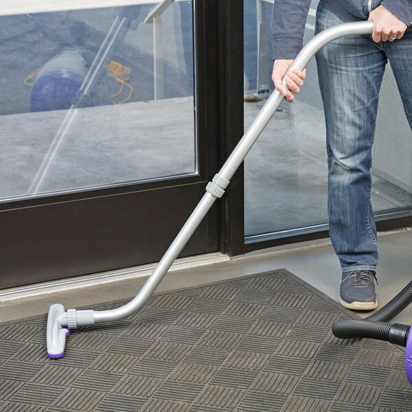 A person using a ProTeam telescoping wand to vacuum a carpeted floor.
