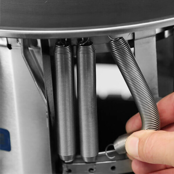 A close-up of a hand adjusting a spring inside a stainless steel heated plate dispenser.