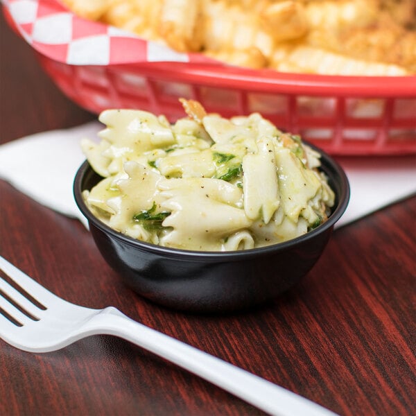 A bowl of pasta with sauce and a Solo black wide sauce portion cup next to a basket of french fries.