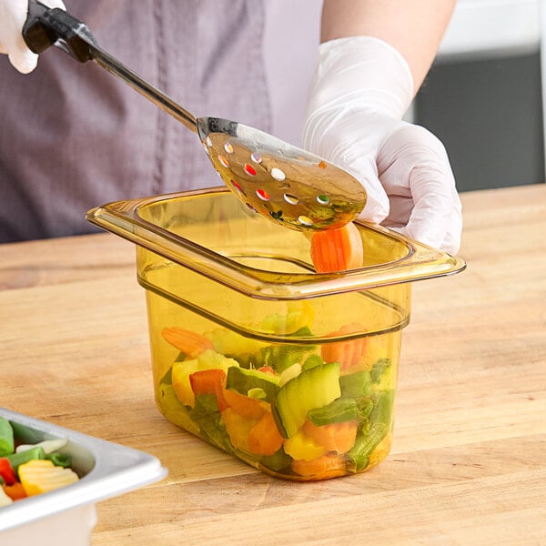 A person putting a carrot into a Cambro amber plastic food container.