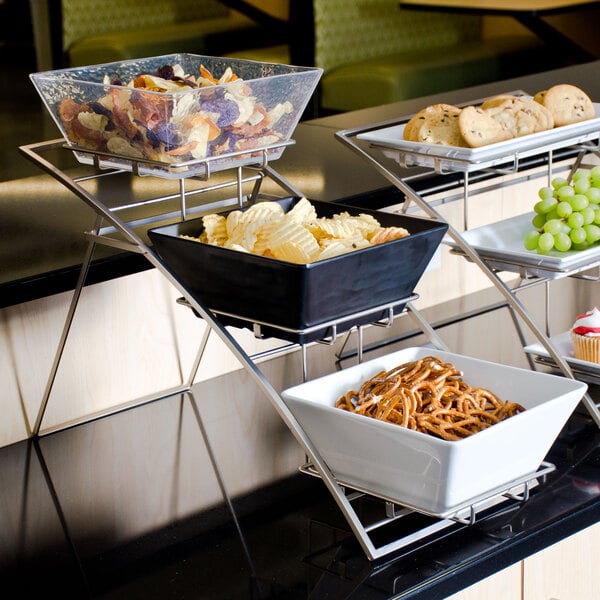 A medium chrome three-tier display stand with bowls of snacks on a hotel buffet table.