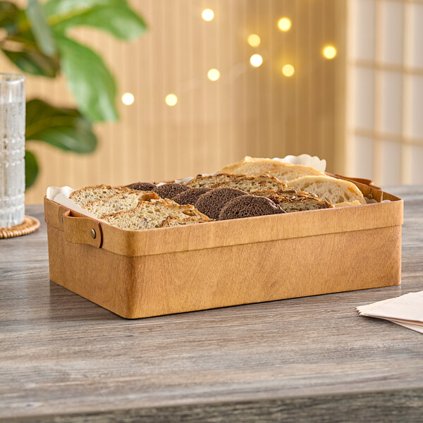 An American Metalcraft rectangular poplar wood basket filled with bread on a table in a bakery display.