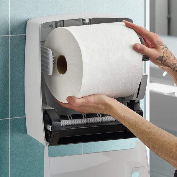 A large white hardwound paper towel roll being loaded into a wall-mounted dispenser.