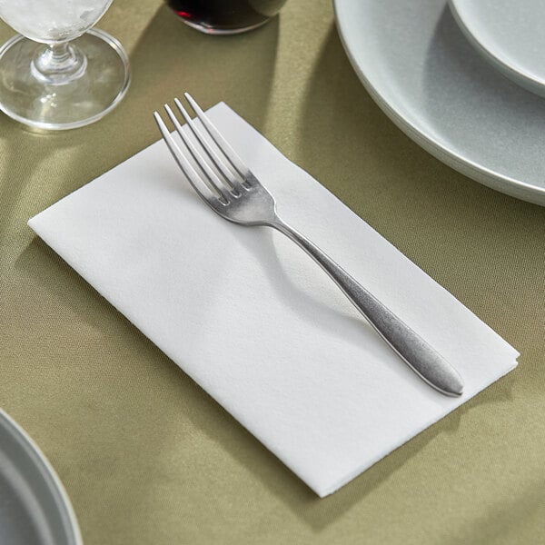 A fork and knife on a white linen-feel dinner napkin on a white plate.