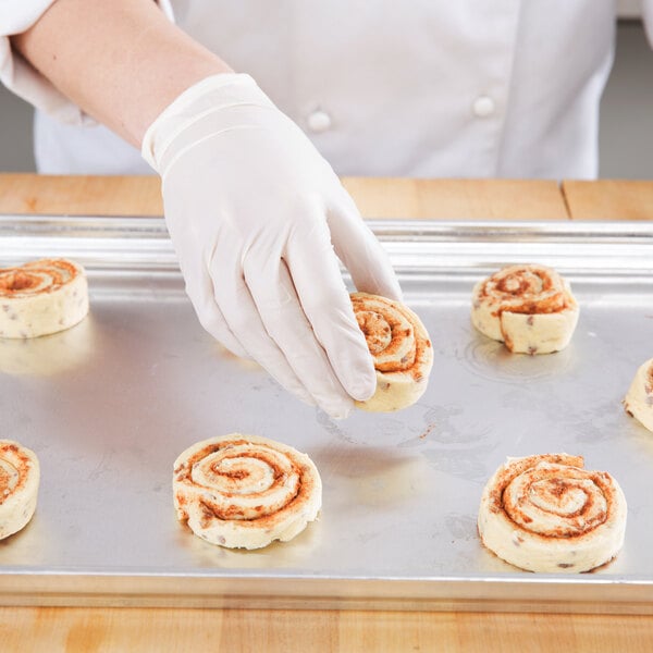 A person in white gloves holding a Chicago Metallic aluminum sheet pan with a cinnamon roll.