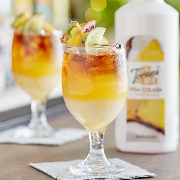 A glass of yellow Torani Pina Colada drink with ice and fruit.