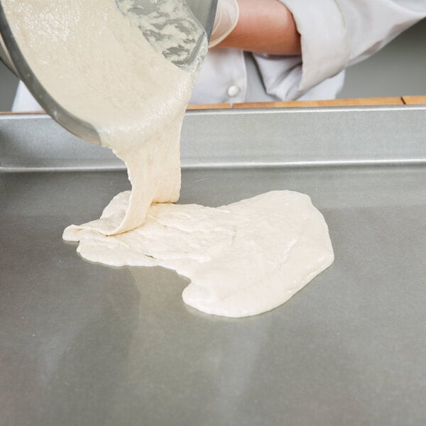 A person pouring dough into a Chicago Metallic sheet cake pan with a wire in rim.