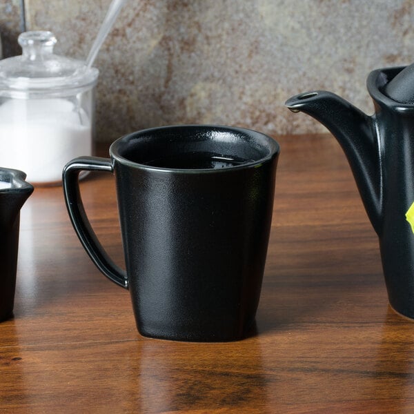 A black Hall China mug filled with liquid on a wooden surface.