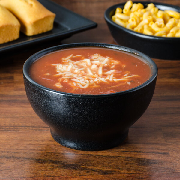 A black china bowl of chili on a table with cornbread.
