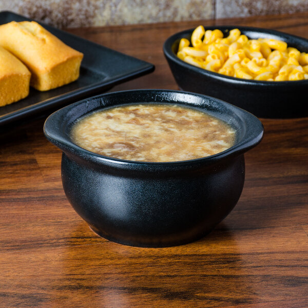 A Hall China black onion soup bowl filled with soup on a table.