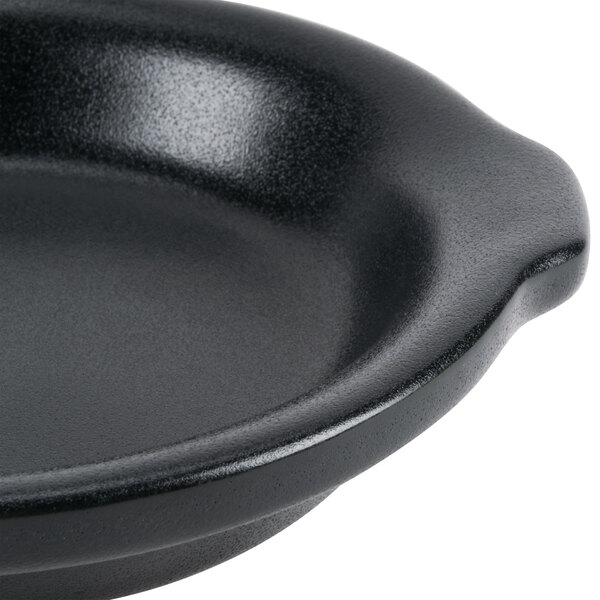 A close up of a black Hall China au gratin dish with a handle.