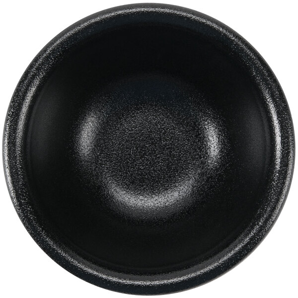 A close-up of a black Hall China sauce dish.