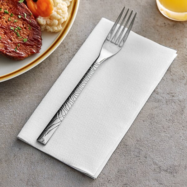 A fork on a Choice white linen-feel dinner napkin next to a plate of food.