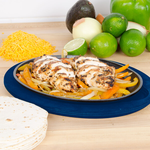 A plate of Lodge oval cobalt blue wood underliner with chicken fajitas and tortillas on it next to a lime half.