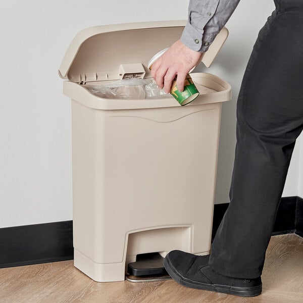 A person putting a can into a Rubbermaid Slim Jim trash can.