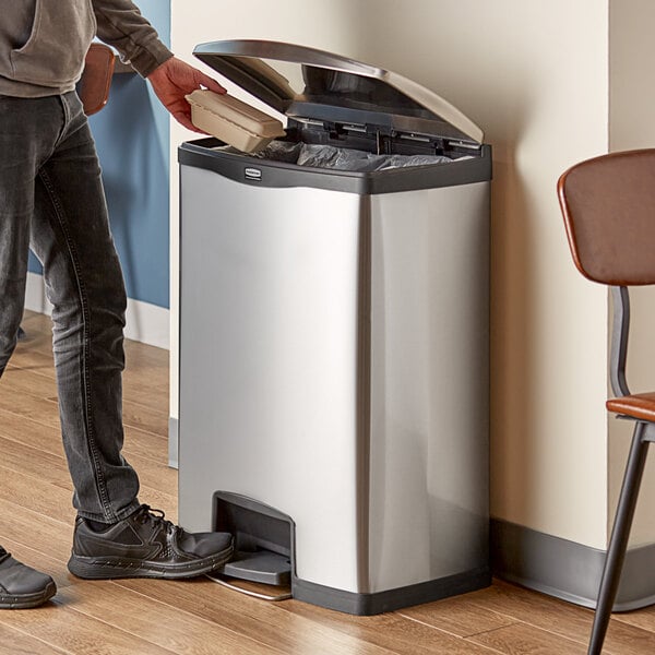 A man using a Rubbermaid Slim Jim stainless steel black accent step-on trash can.