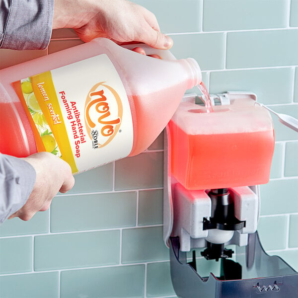 A person pouring Noble Chemical Novo foaming hand soap into a soap dispenser.