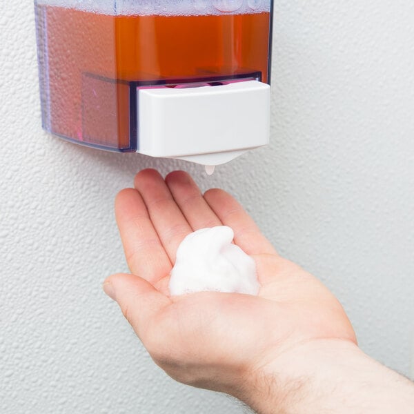 A person dispensing foaming hand soap from a wall-mounted dispenser onto their hand.
