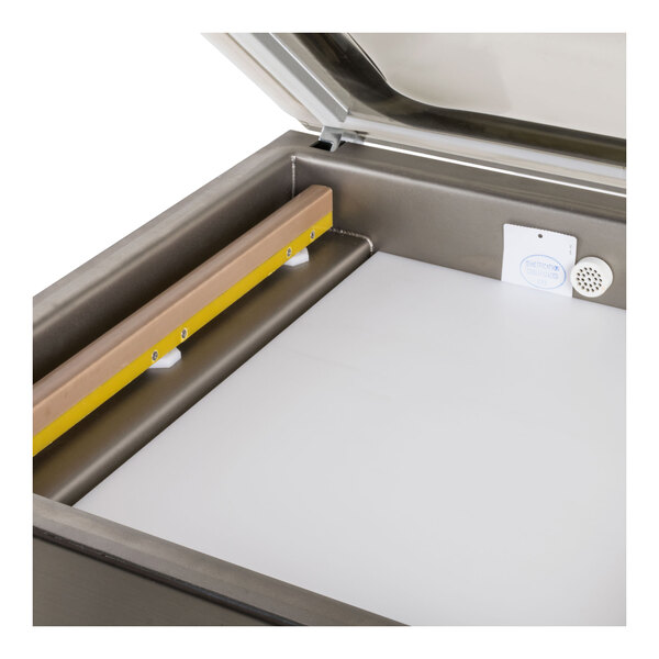 A close-up view of the interior of a packaging machine with a flat white filler plate and a wooden bar along one side.