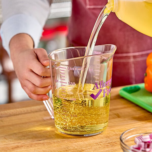 A person pouring liquid into a purple Cambro measuring cup.