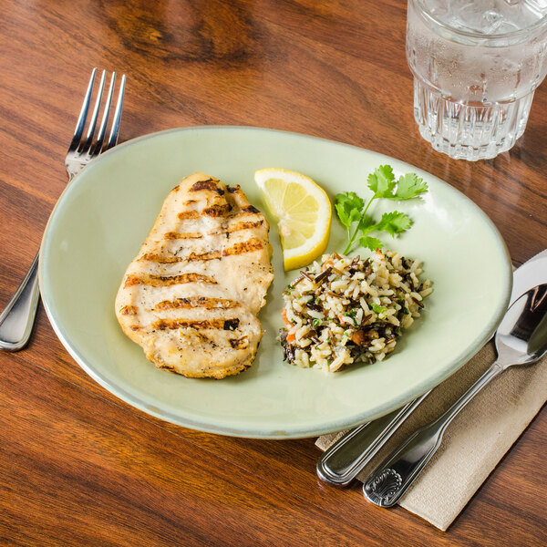A Tuxton Artisan Sagebrush china plate with grilled chicken, rice, and a lemon wedge on a table.