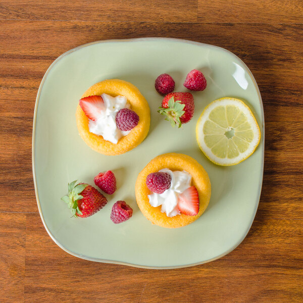 A Tuxton Artisan Sagebrush china plate with three small desserts topped with strawberries and cream.