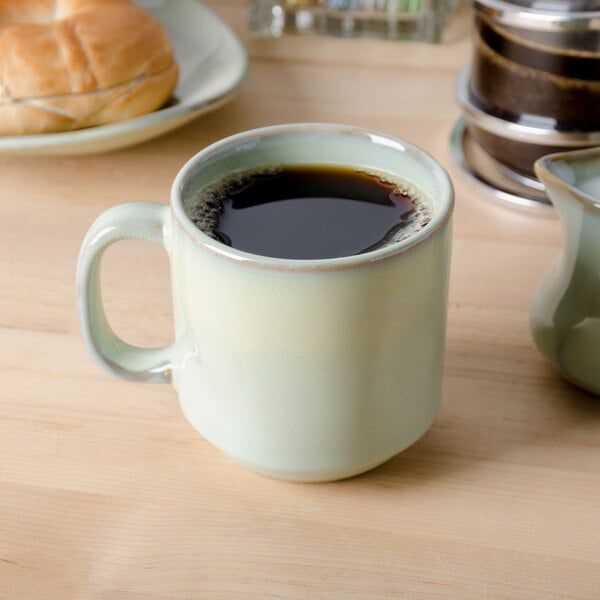 A Tuxton Yukon china mug filled with coffee on a table with a plate of bread.