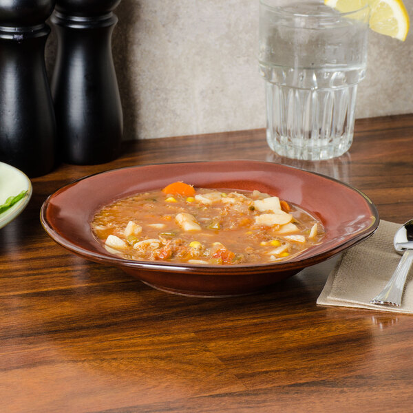 A TuxTrendz Artisan Red Rock china soup bowl filled with soup on a table with a spoon and a glass of water.