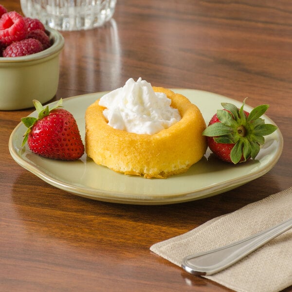 A Tuxton Artisan Sagebrush china plate with a small round pastry and strawberries with whipped cream on it.