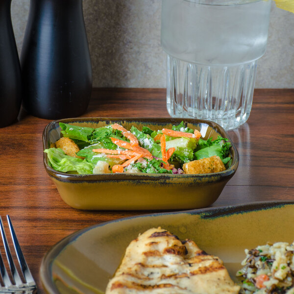 A rectangular bowl filled with salad on a table next to a glass of water.