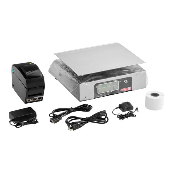 A digital price computing scale with a stainless steel platform, a thermal printer, a roll of paper, power adapters, and various connecting cables arranged on a white background.