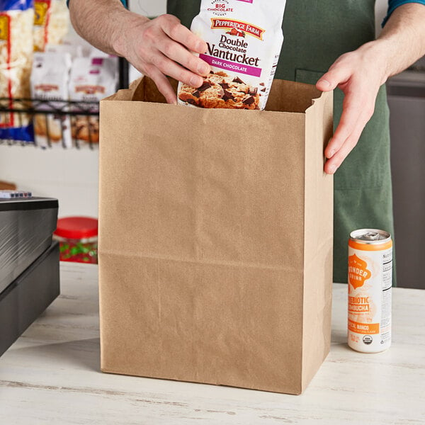 A person putting a brown paper bag of food into a Duro paper barrel sack with a handle.