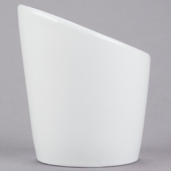 A Tuxton bright white tall slanted side dish with a curved edge on a gray surface.