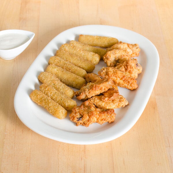 A Tuxton eggshell oval china platter with fried chicken and fries and a bowl of liquid.