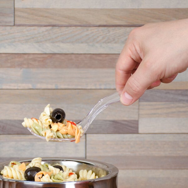 A hand holding a Fineline clear plastic serving spoon full of pasta.