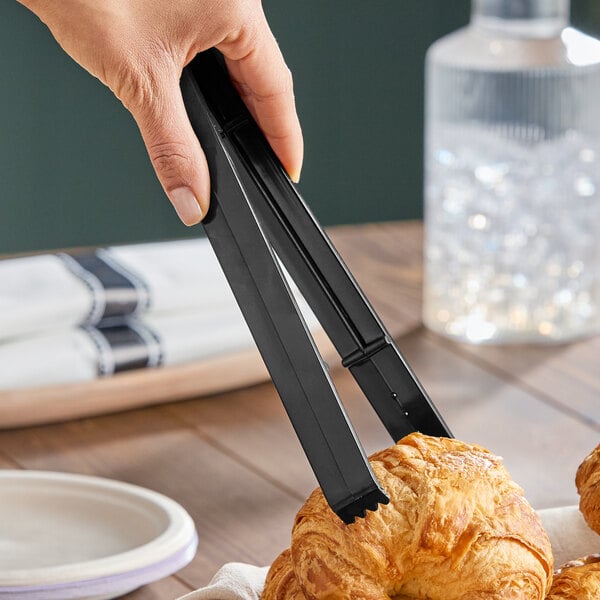 A pair of black plastic heavy-duty serving tongs being used to pick up a croissant.