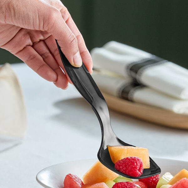 A black plastic serving spoon being used to serve fruit.
