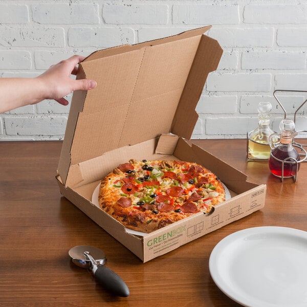 Pizza with vegetables in box with a pizza cutter beside it