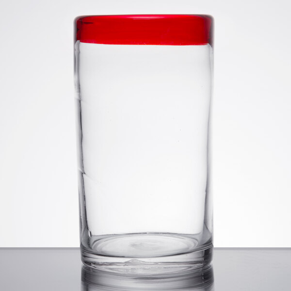 A clear Libbey cooler glass with a red rim on a table.