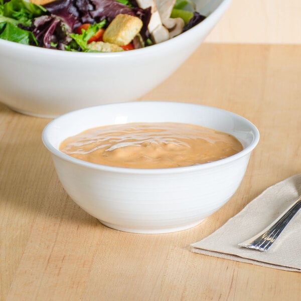 A Tuxton bright white china nappie bowl filled with soup next to a bowl of salad on a table.