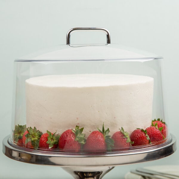 A close-up of a cake with strawberries on top covered by a Cambro clear dome cover.