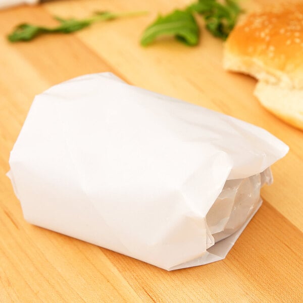 A 12" x 15" white wet wax paper wrapped sandwich on a wooden table.