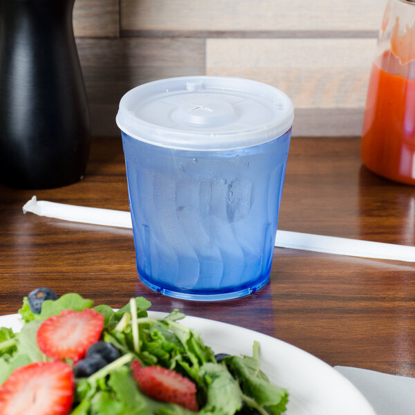 A blue Dinex SAN plastic tumbler filled with water next to a plate of salad.
